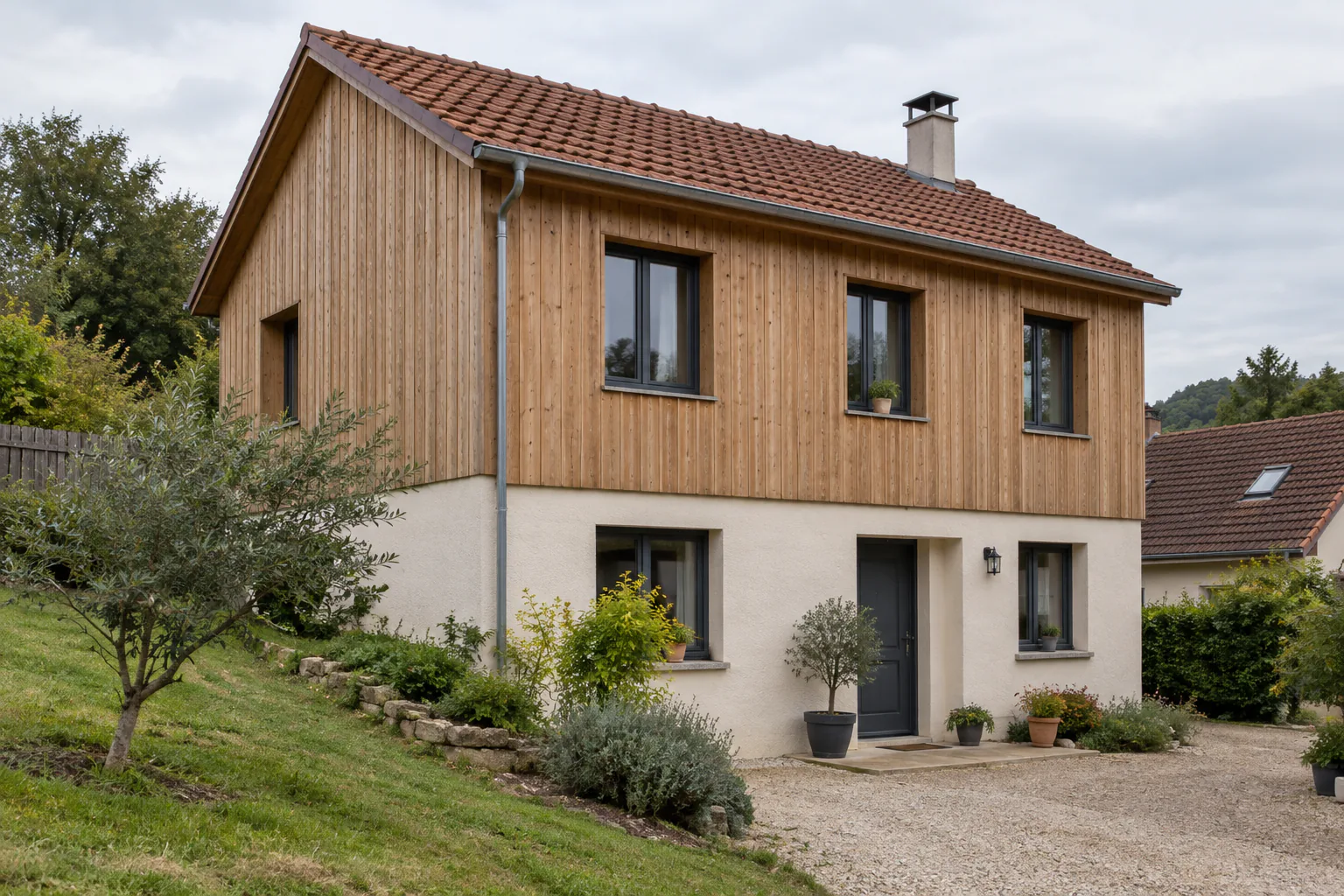 Maison à étage supérieur en bardage bois Le niveau supérieur d’une maison est habillé de bois vertical, au-dessus d’un rez-de-chaussée clair.