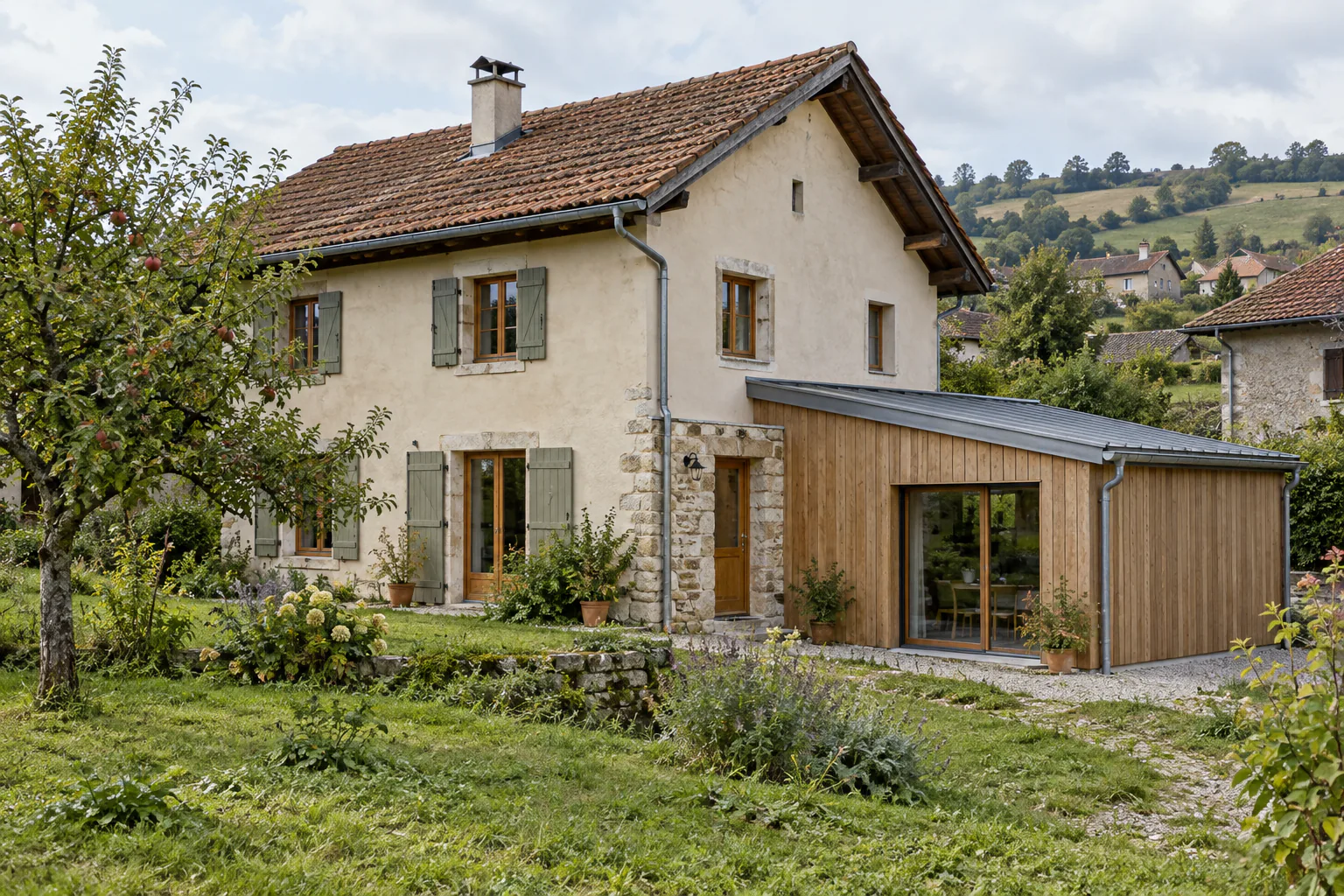 Maison en pierre prolongée par un volume bois Une maison ancienne aux volets clairs possède une extension latérale en bois avec baie vitrée et toit incliné.