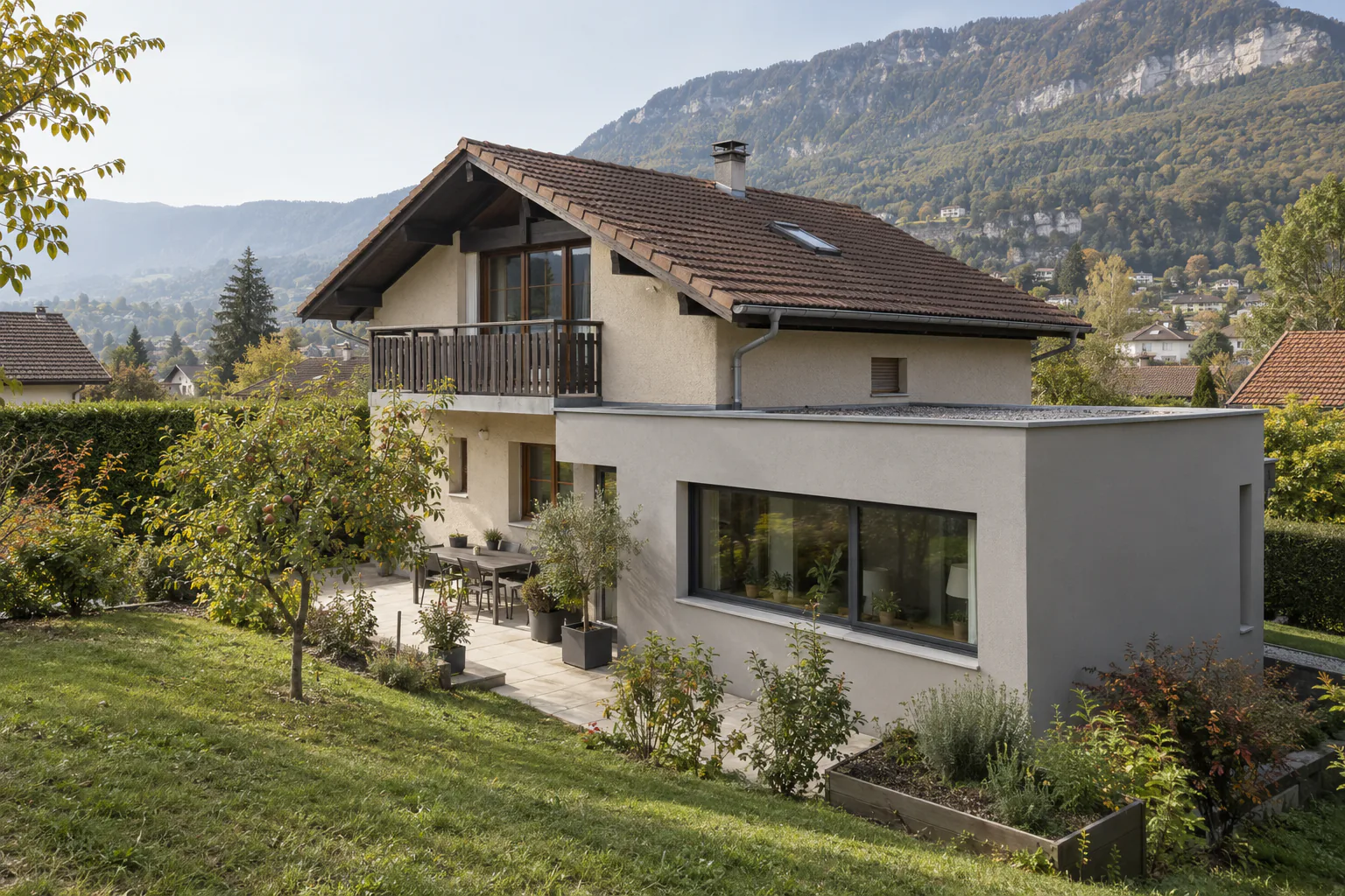 Maison avec balcon et extension claire en contrebas Une maison avec balcon en bois possède une extension claire au niveau du jardin, devant une pelouse en pente.