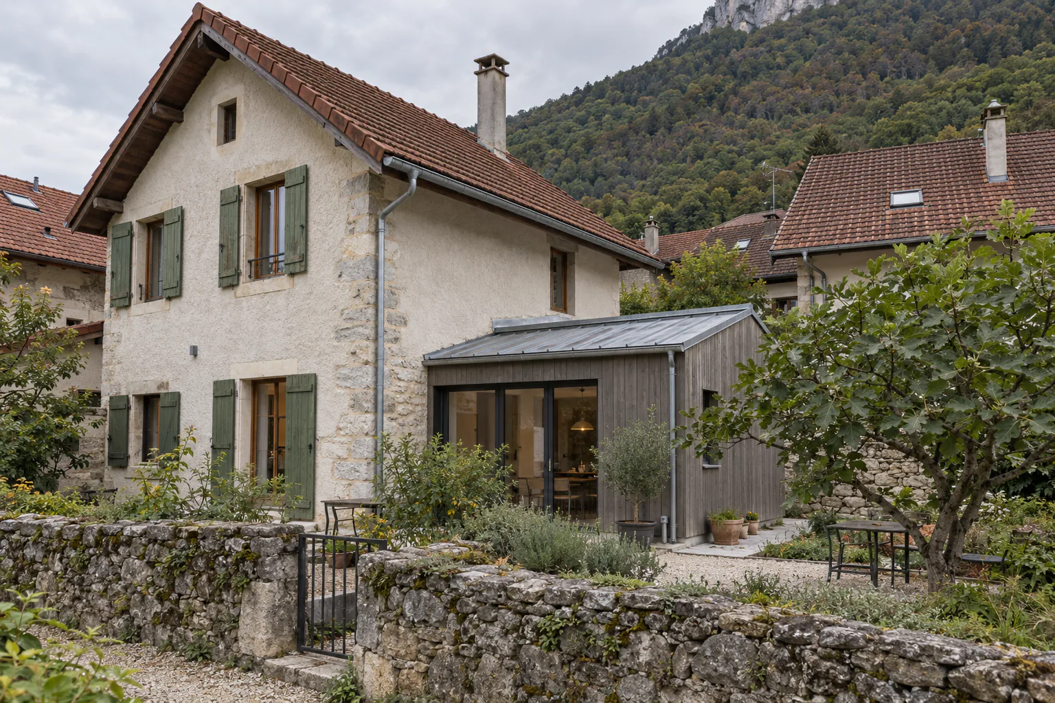 Maison de pierre et petite extension bois grisée Une petite extension à bardage grisé et toit métallique prolonge une maison en pierre aux volets verts.