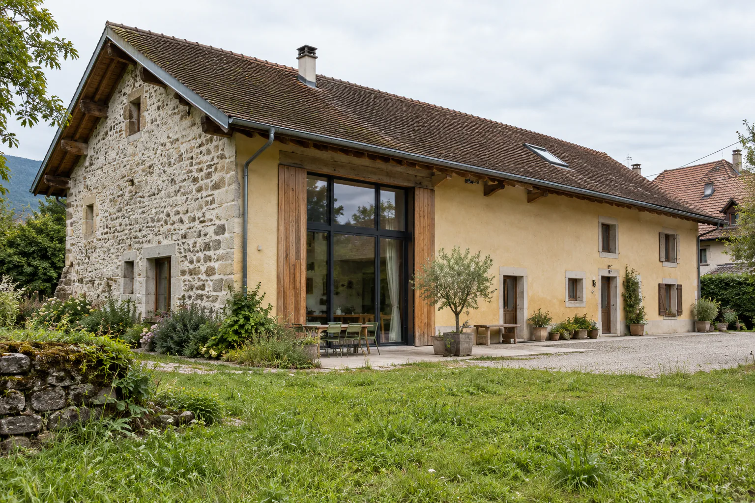 Ancienne bâtisse et grande ouverture vitrée dans le pignon Une longue bâtisse associe enduit clair et pierre apparente, avec une grande baie verticale sous le pignon.