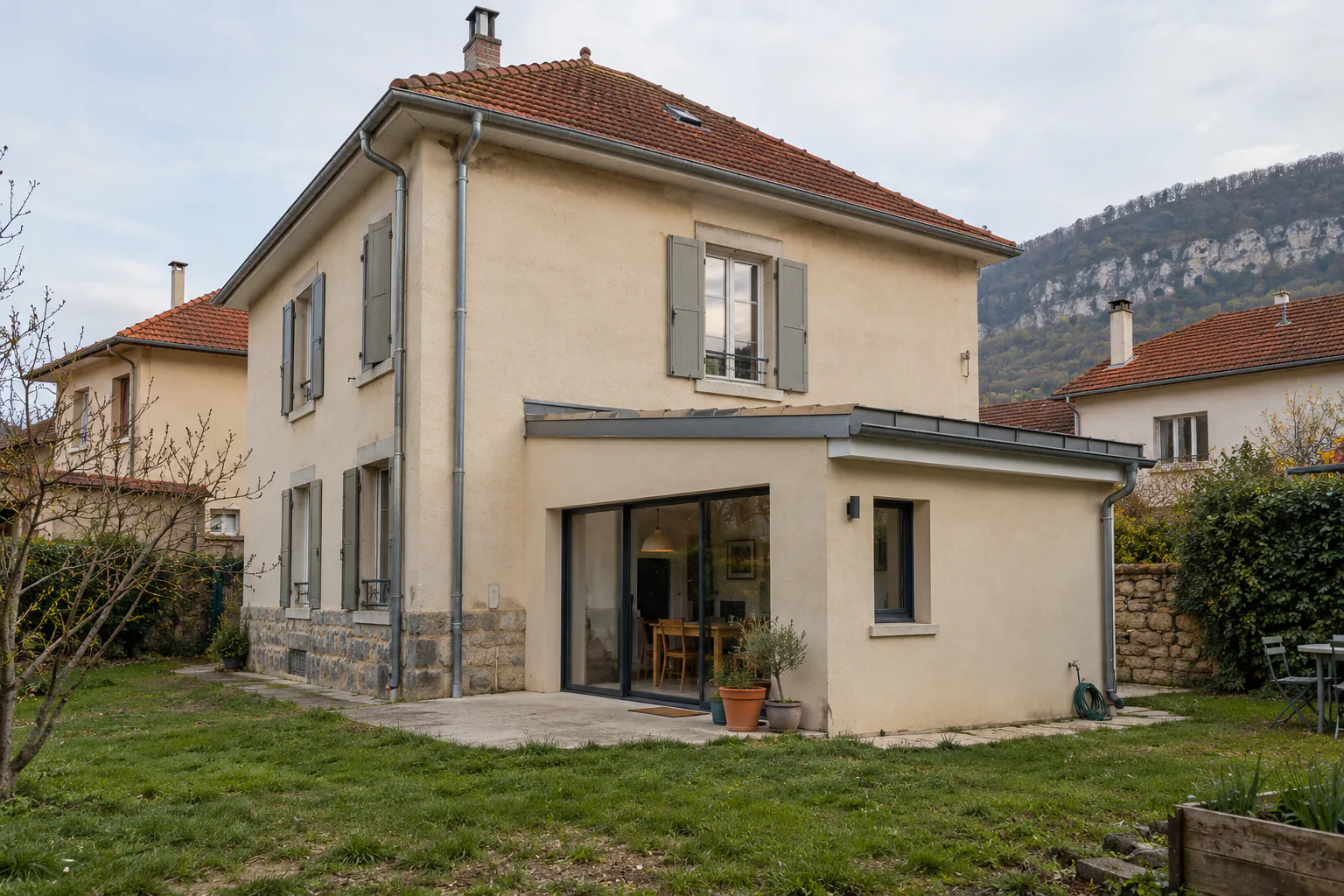 Maison à étage et extension claire sur pelouse Une petite extension claire à toit plat s’ouvre sur le jardin par une large baie, au pied d’une maison à étage.