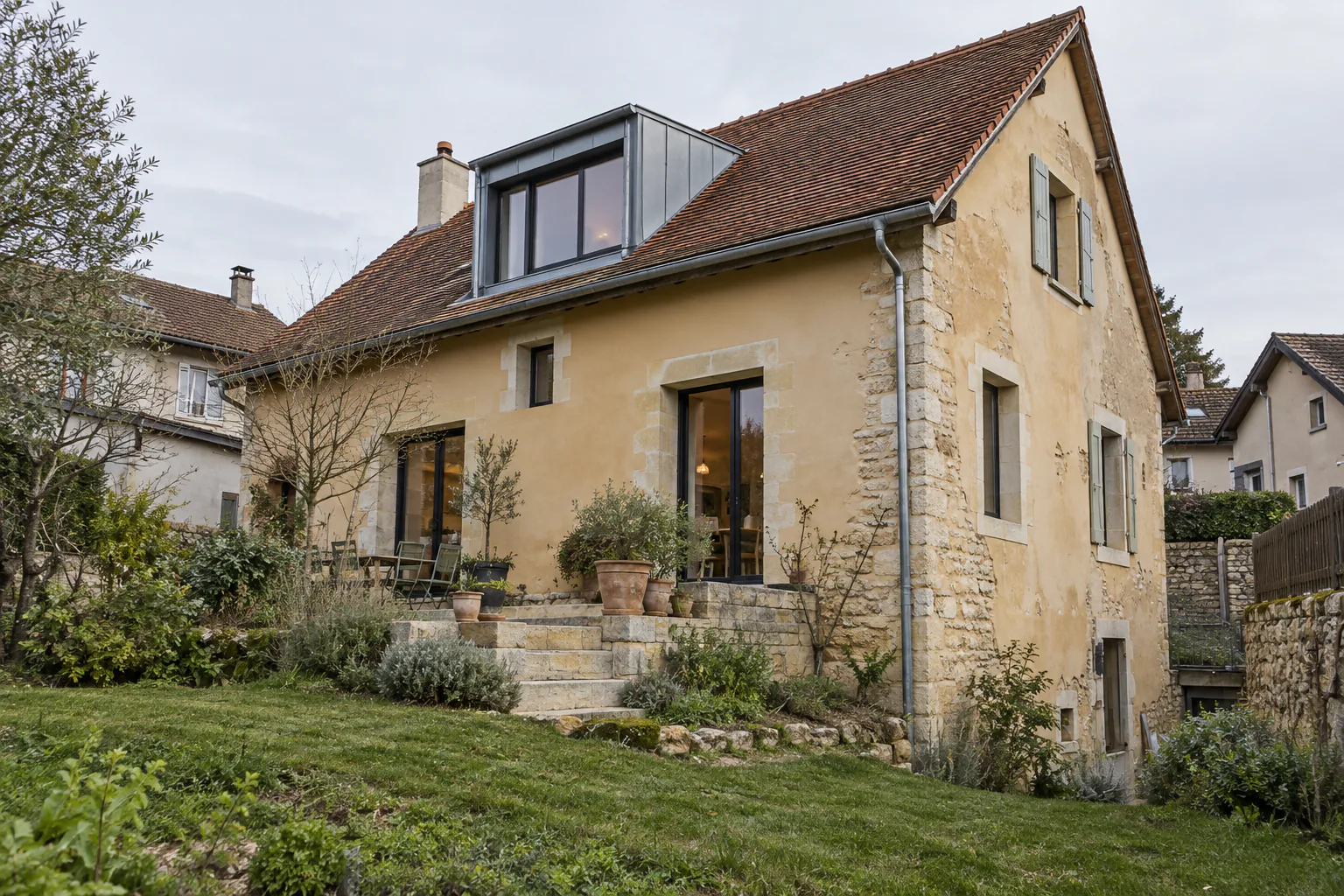 Maison en pierre et grande lucarne métallique Une grande lucarne vitrée habillée de métal occupe la toiture d’une maison à façade patinée et angle en pierre.
