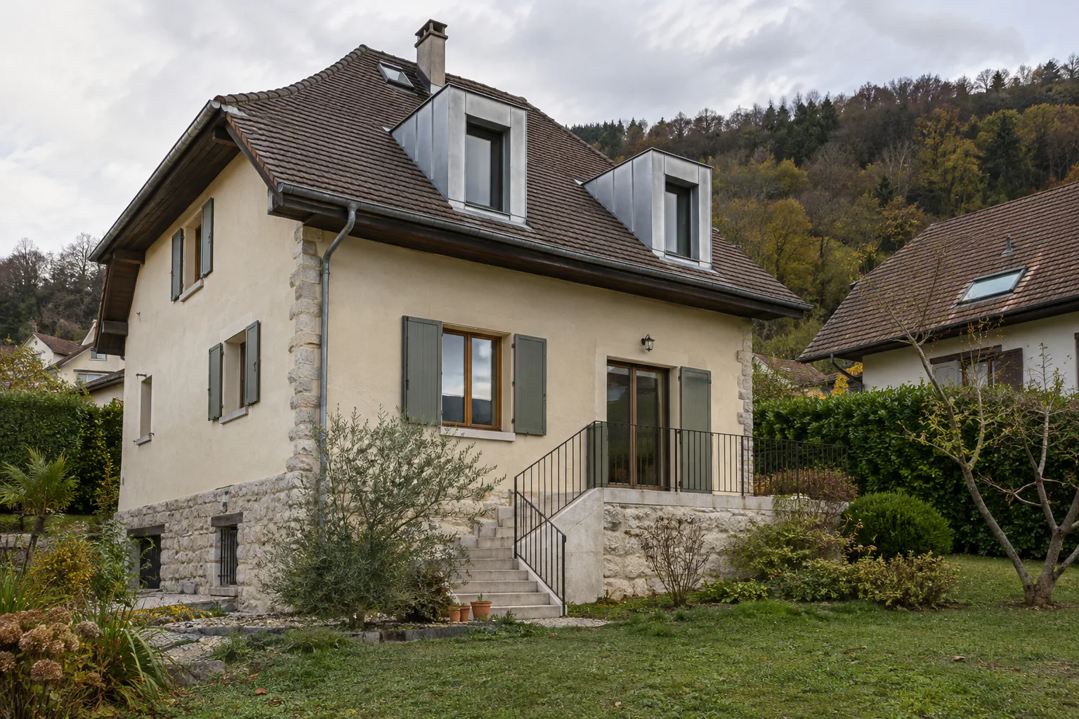 Maison ancienne à deux lucarnes et escalier de pierre Deux lucarnes percent le toit d’une maison ancienne, dont l’entrée est accessible par un escalier en pierre à garde-corps.
