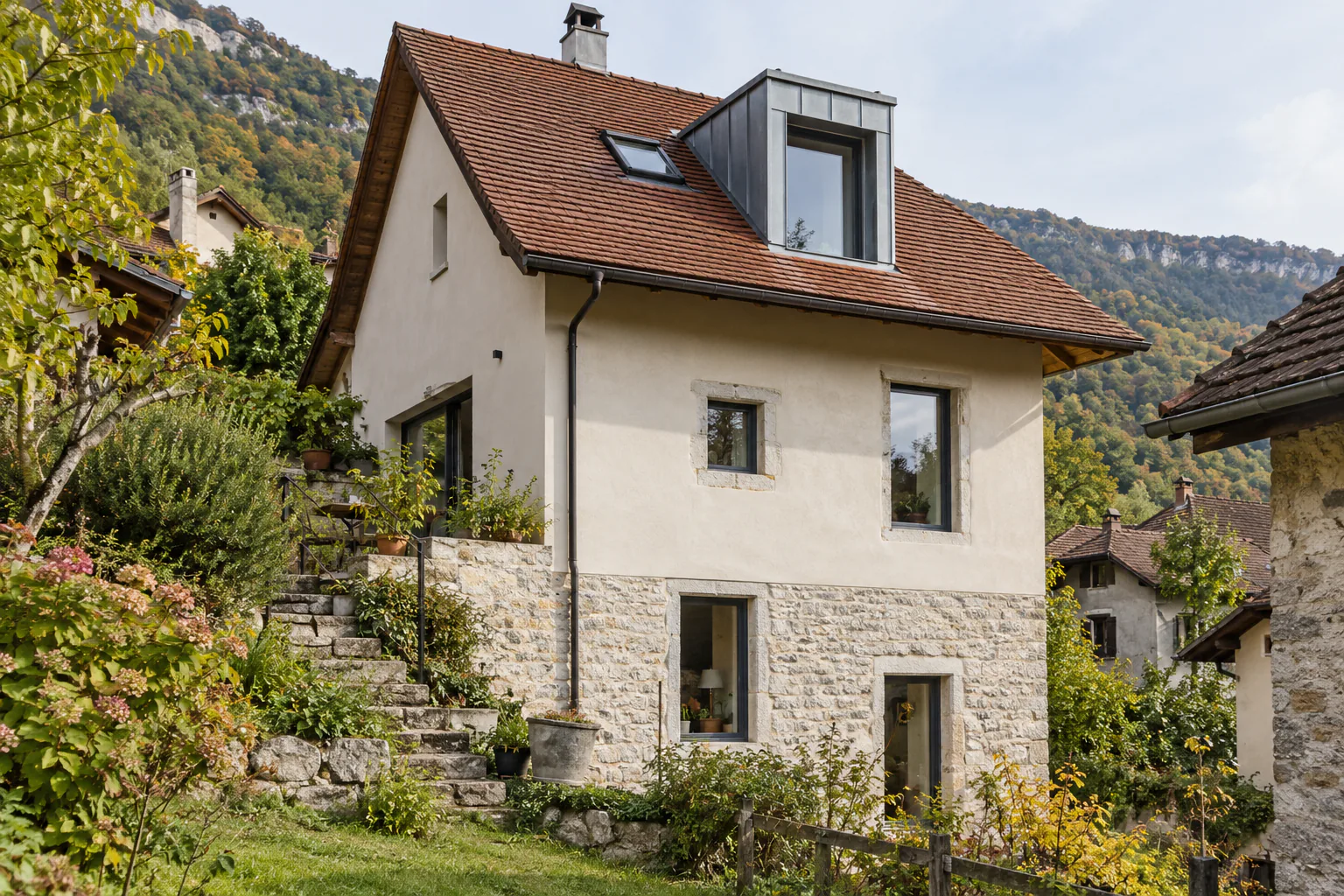 Maison sur pierre avec lucarne verticale métallique Une lucarne haute habillée de métal se détache sur le toit d’une maison claire au soubassement de pierre.