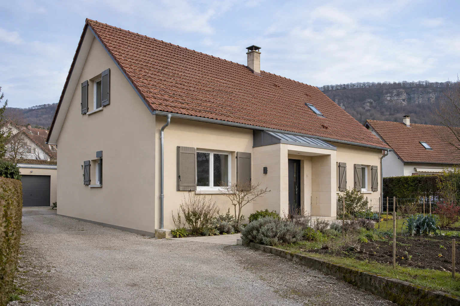 Maison basse avec entrée abritée sous toiture métallique Une entrée en retrait sous une petite toiture métallique anime la façade claire d’une maison aux volets gris.