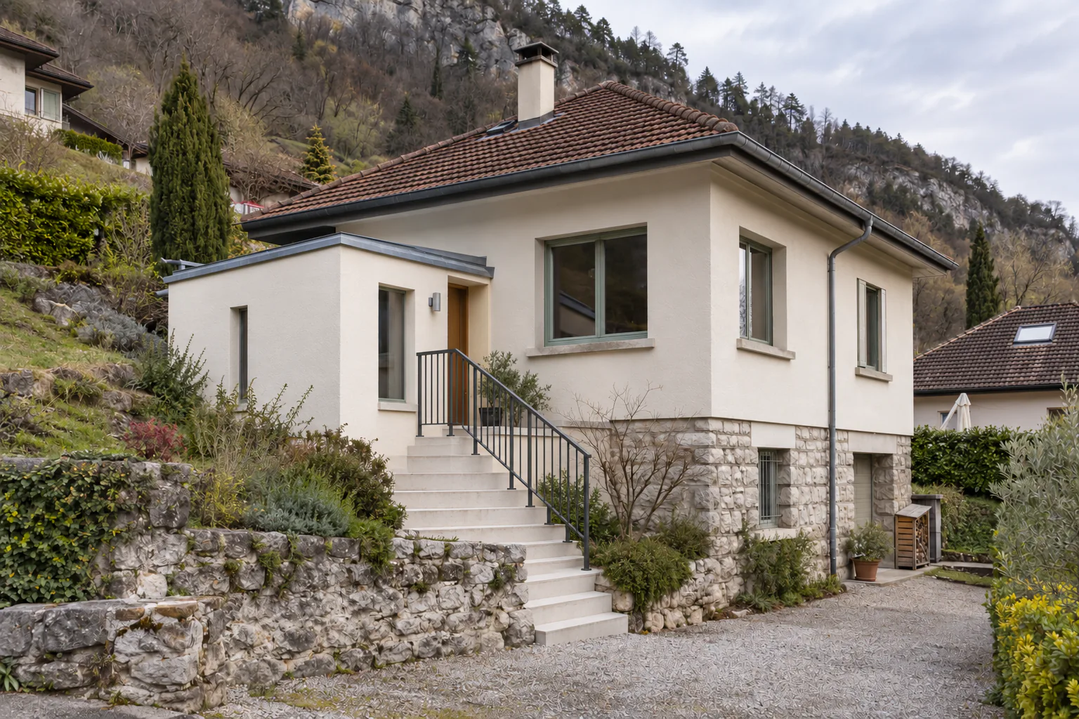 Maison claire et escalier protégé sur terrain pentu Un escalier extérieur muni d’un garde-corps monte vers une petite entrée claire, sur le côté d’une maison en pente.