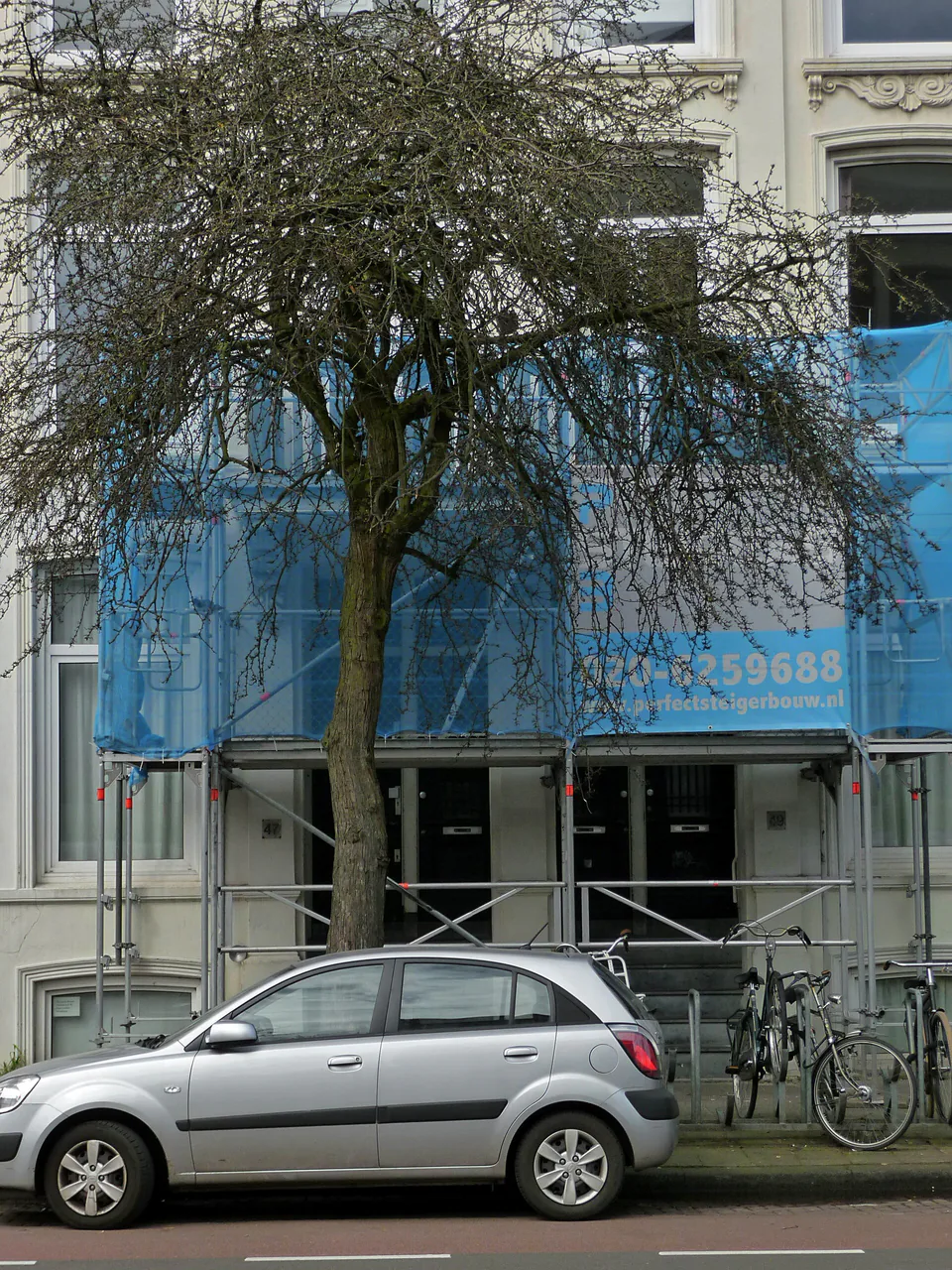 Façade urbaine sous une bâche bleue Échafaudage couvert d'une bâche bleue devant une façade et une voiture stationnée.