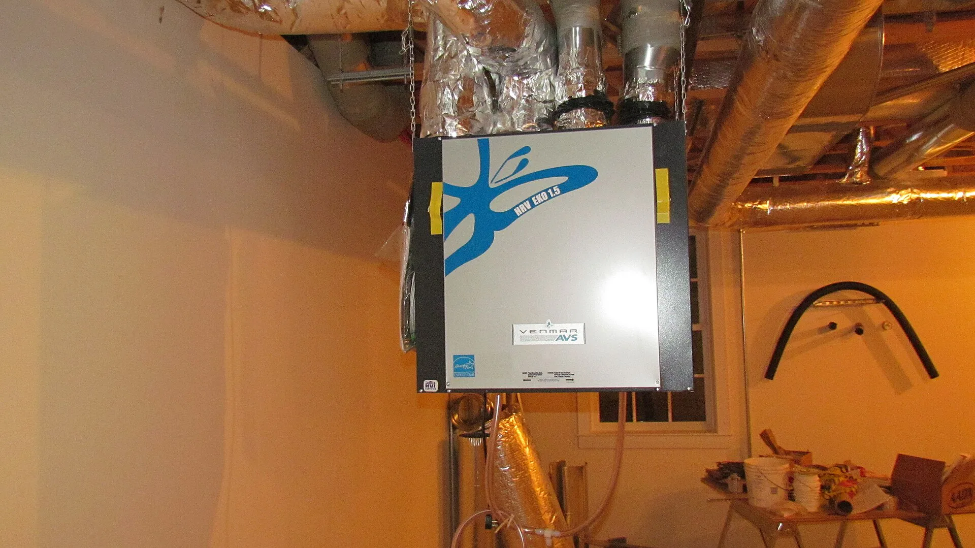 Ventilation raccordée à des gaines isolées Caisson de ventilation suspendu dans un local, raccordé à plusieurs gaines métalliques isolées.