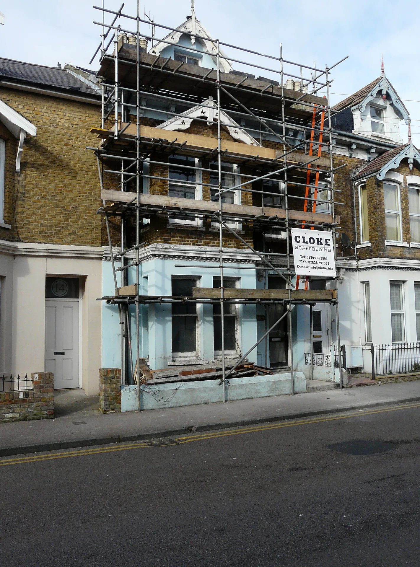 Maison urbaine avec toiture en travaux Échafaudage couvrant la façade et la toiture ouverte d'une maison en bord de rue.