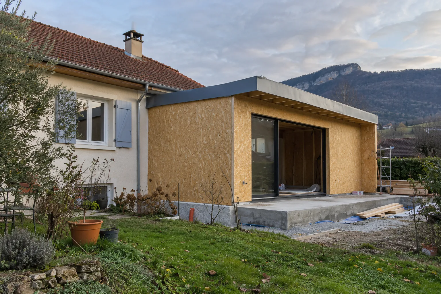Extension avec panneaux bois et baie ouverte Volume d'extension à toiture plate revêtu de panneaux bois, avec grande ouverture devant le jardin.