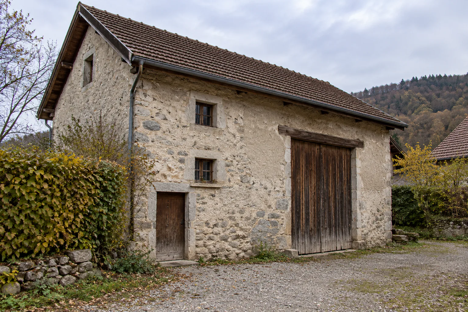 Avant : Petit bâtiment en pierre avec grande porte de grange fermée et toit en tuiles.