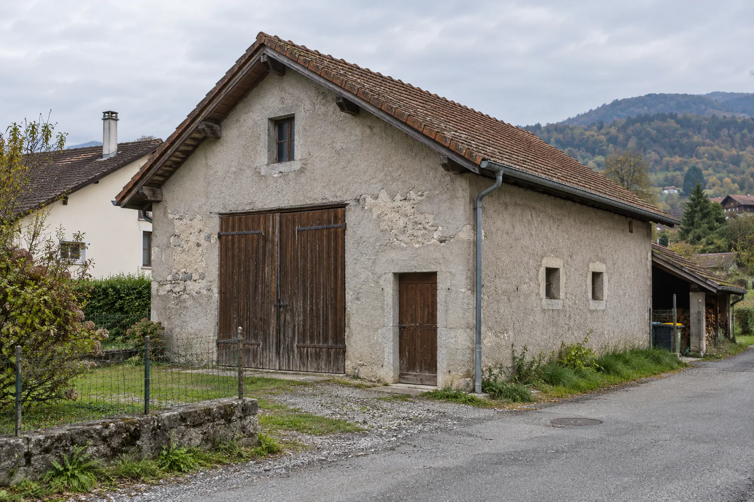 Avant : Bâtiment bas à toit en tuiles avec grande porte en bois et appentis sur le côté.