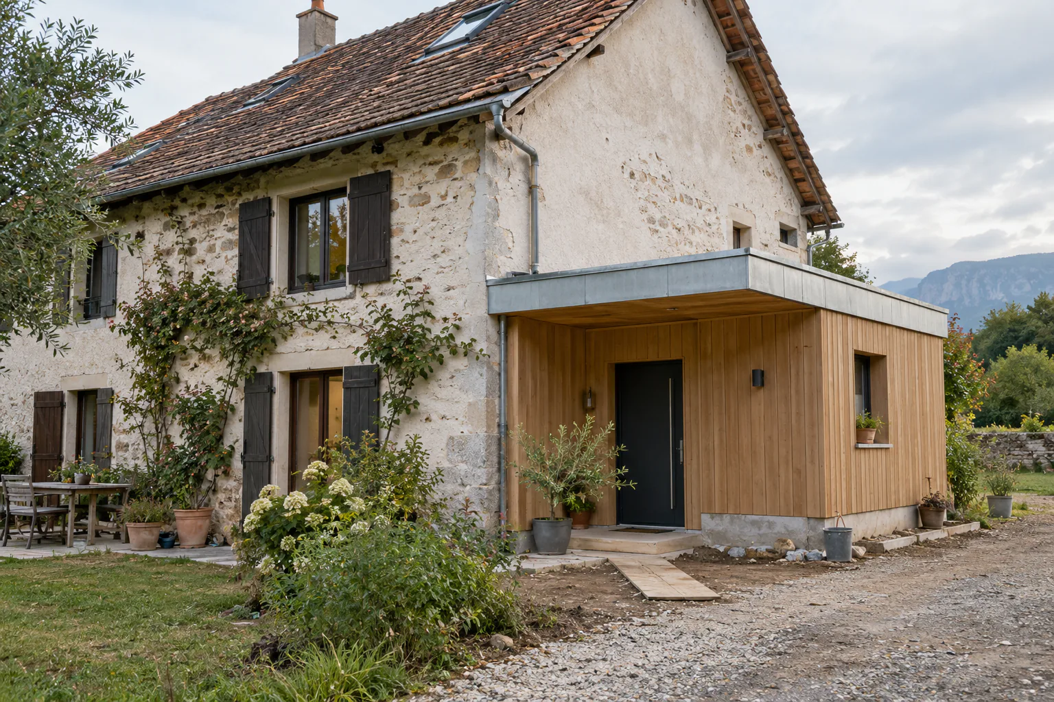Maison en pierre et enduit ancien, prolongée par une petite entrée en bardage bois.