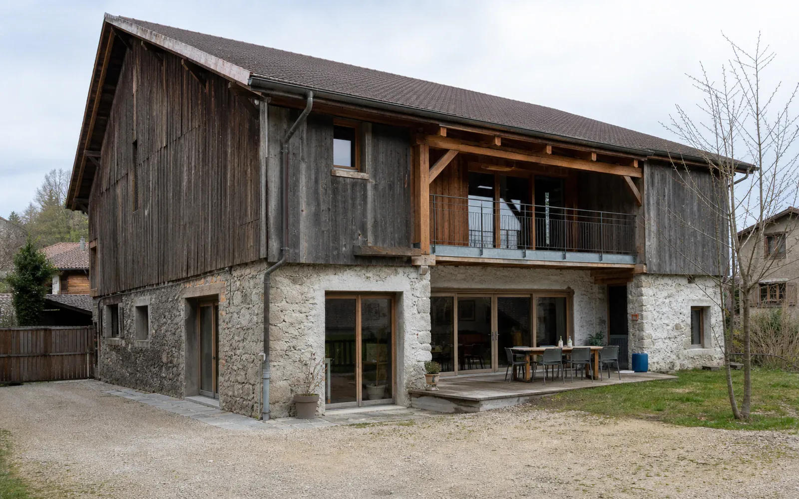 Grange à bardage bois avec balcon Grand bâtiment à étage en bois et pierre avec balcon et baies vitrées au rez-de-chaussée.