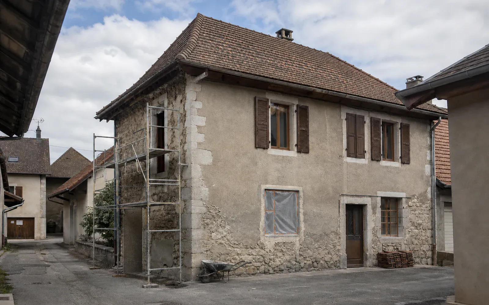 Maison en pierre aux volets bruns Maison à étage en pierre avec volets bruns et ouvertures basses partiellement protégées.