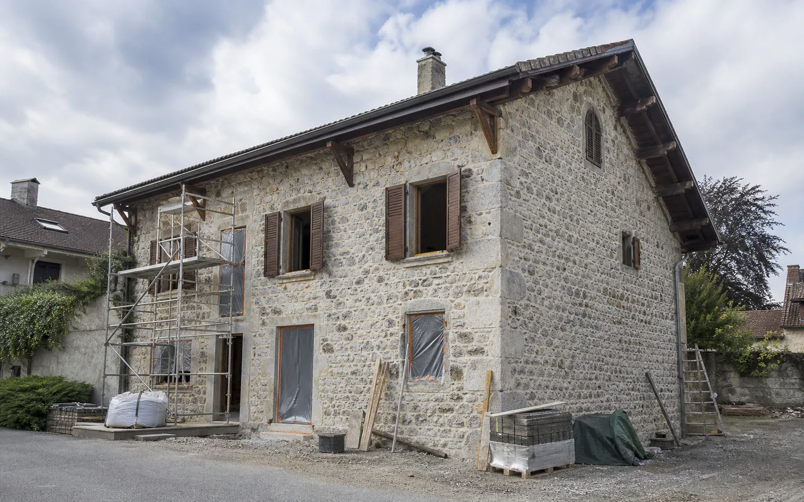 Façade en pierre devant un échafaudage Maison en pierre avec échafaudage sur une partie de la façade et matériaux au sol.