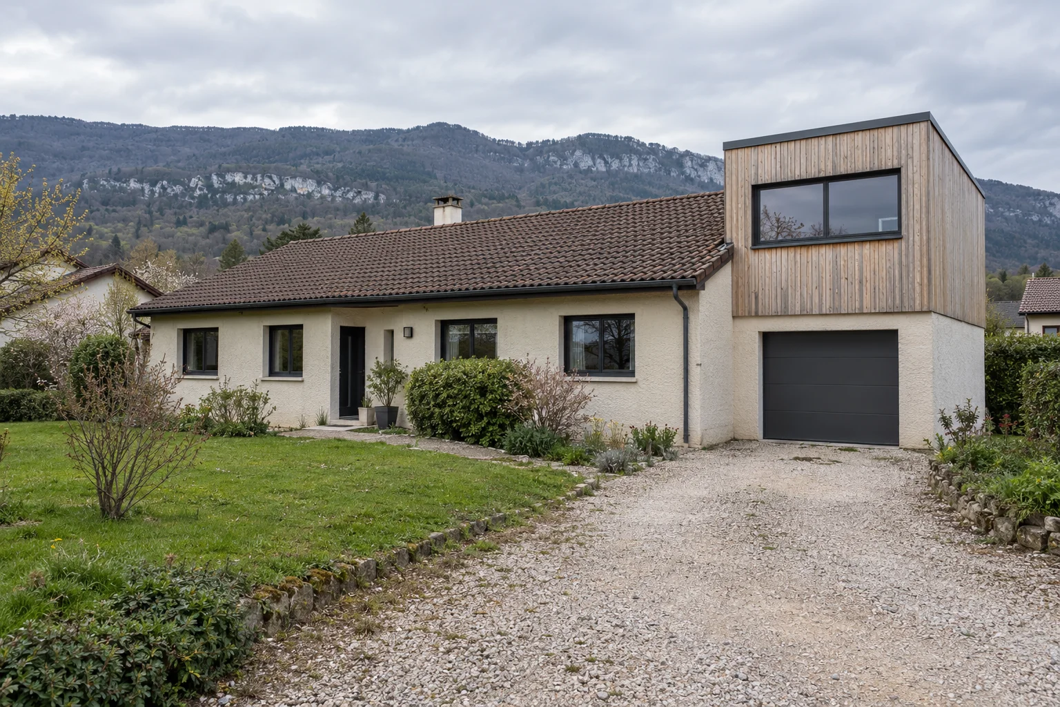 Thoiry — bureau en surélévation au-dessus du garage Une maison de plain-pied à toiture de tuiles, avec un bureau en bardage bois construit au-dessus du garage latéral.